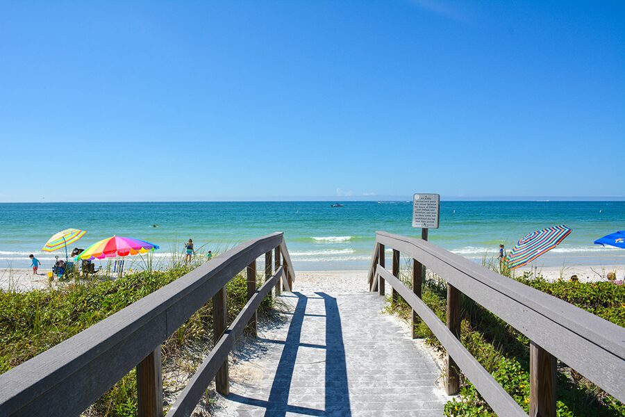 Boardwalk leading to a beach with blue water and blue sky.