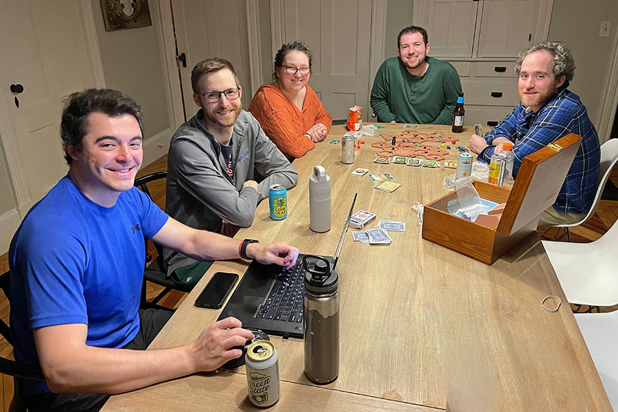 A group poses around a wood table with a laptop and board game